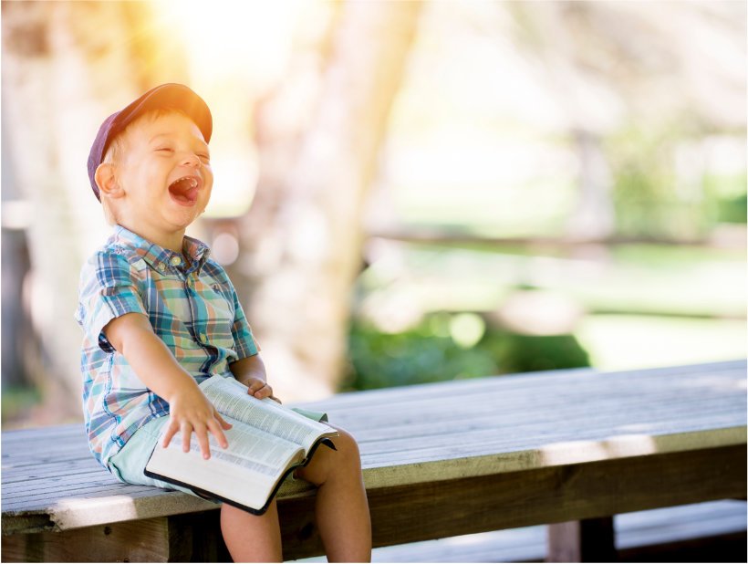 A little boy laughing while reading the Holy Bible